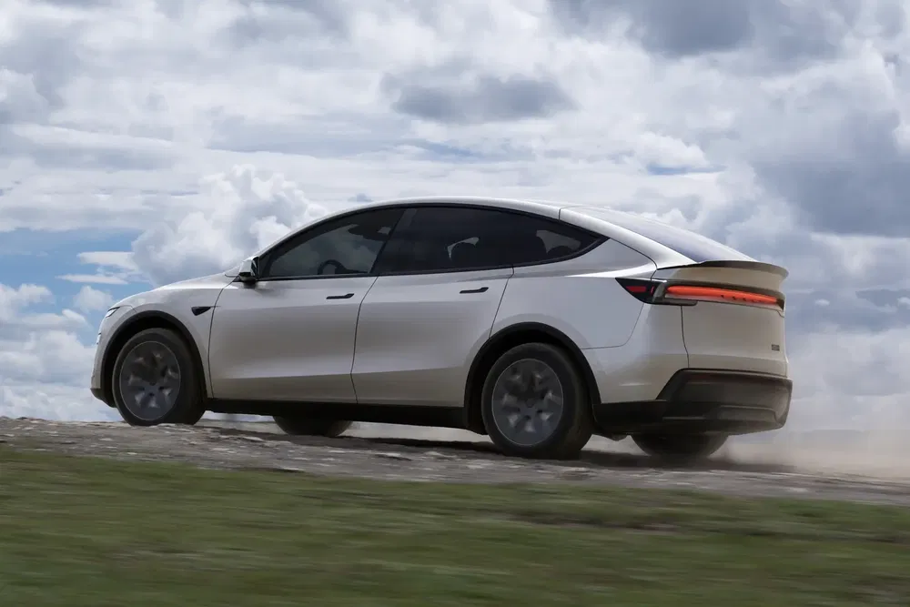 Voiture électrique Tesla Model Y roulant sur un chemin de terre sous un ciel nuageux.