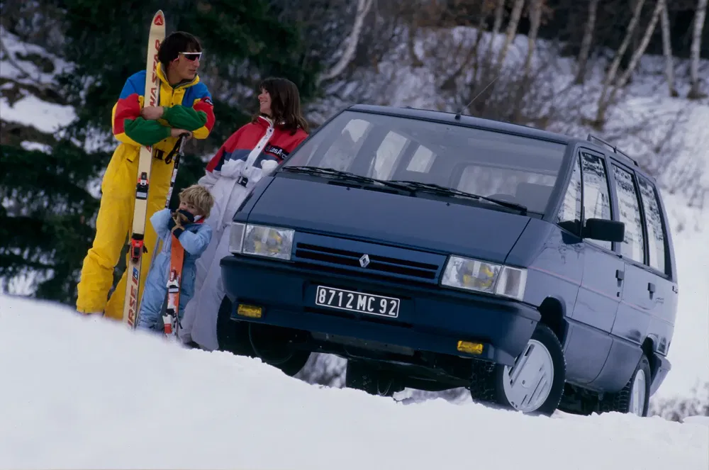 Renault Espace garé dans la neige avec une famille équipée de skis, ambiance hivernale.