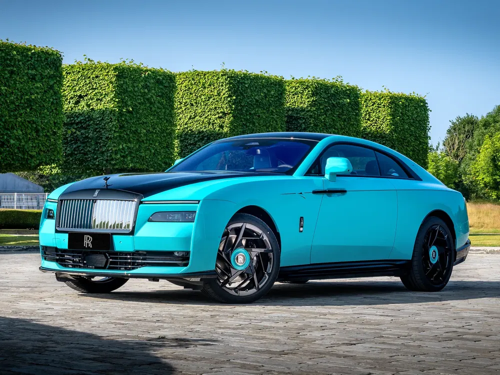 Rolls-Royce Spectre bleue et noire stationnée devant des haies taillées sous un ciel dégagé.