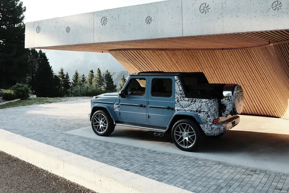 {"fr":"Mercedes-Benz Classe G bleu stationné sous un abri moderne avec un arrière camouflé.","nl":"Blauwe Mercedes-Benz G-Klasse geparkeerd onder een moderne overkapping met gecamoufleerde achterkant."}