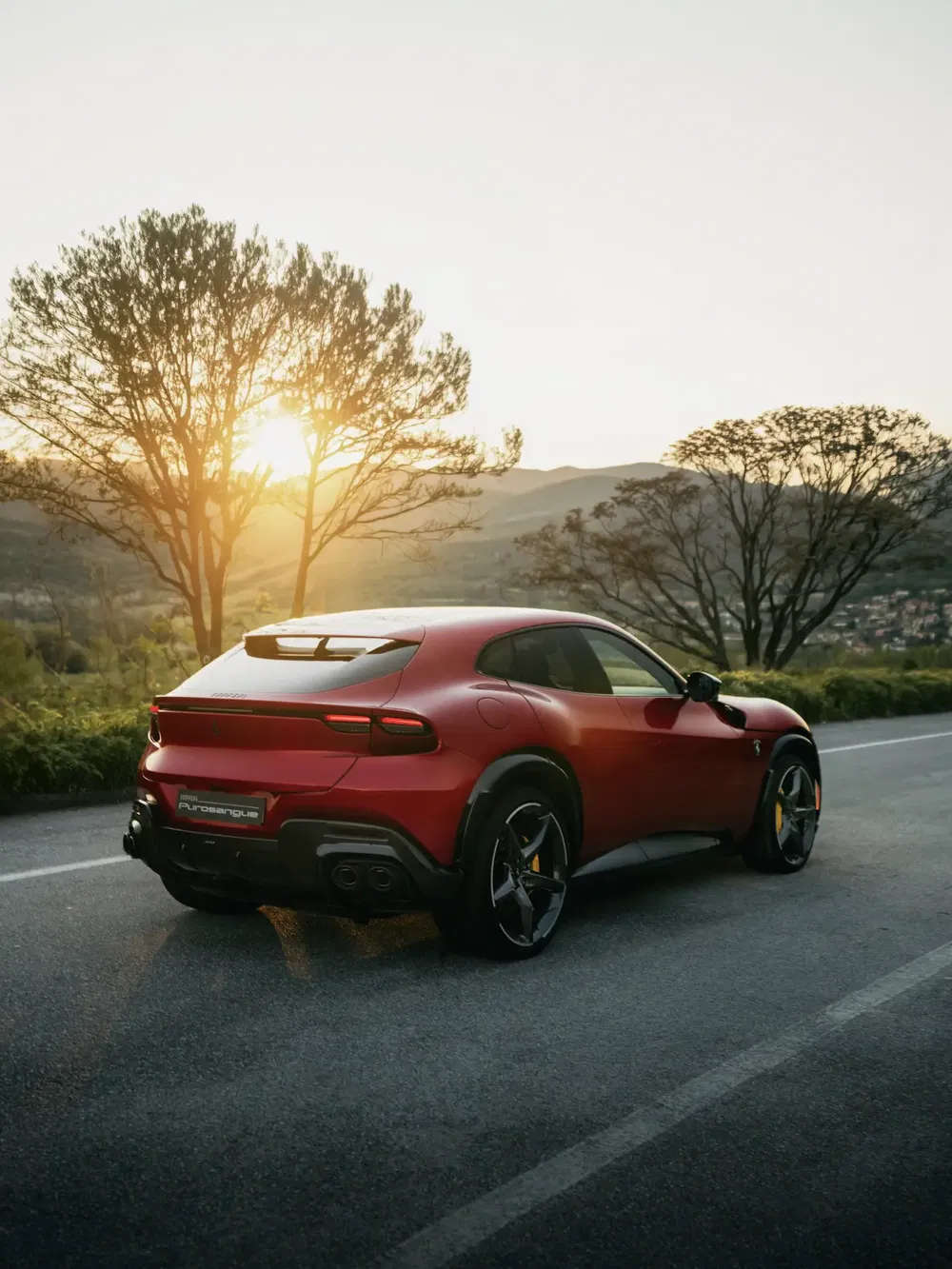 Ferrari Purosangue rouge au coucher du soleil sur route de campagne pittoresque.