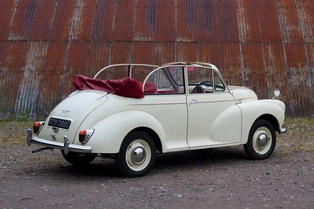 Morris Minor décapotable blanche devant un vieux hangar rouillé.