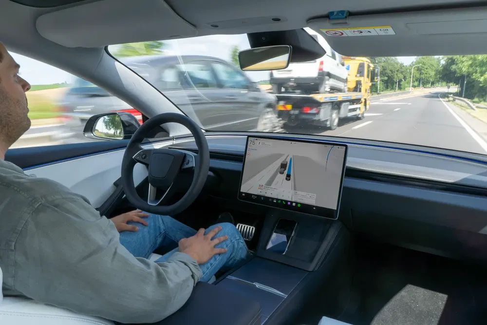 Homme dans une Tesla en mode autonome sur une route avec écran affichant la navigation.
