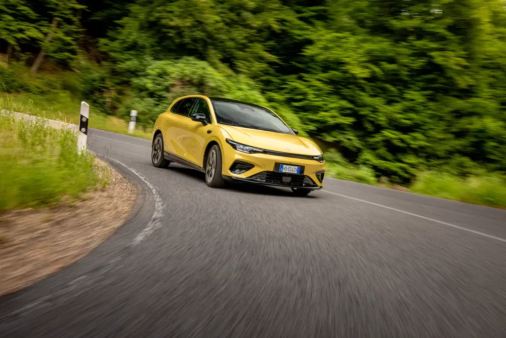 Voiture jaune MG4 traversant une route sinueuse entourée de verdure dense.