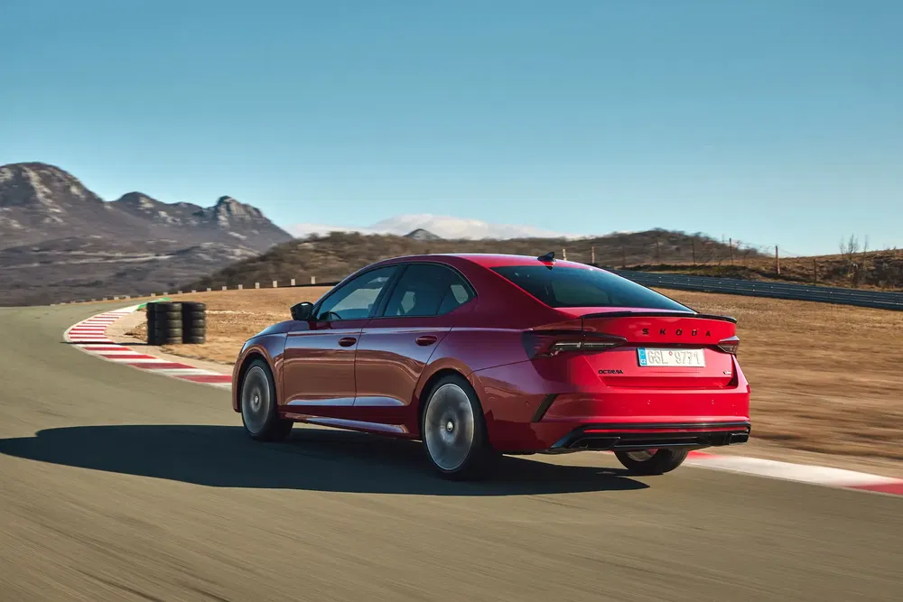 Skoda Octavia rouge sur circuit sinueux avec montagnes en arrière-plan, par temps clair.
