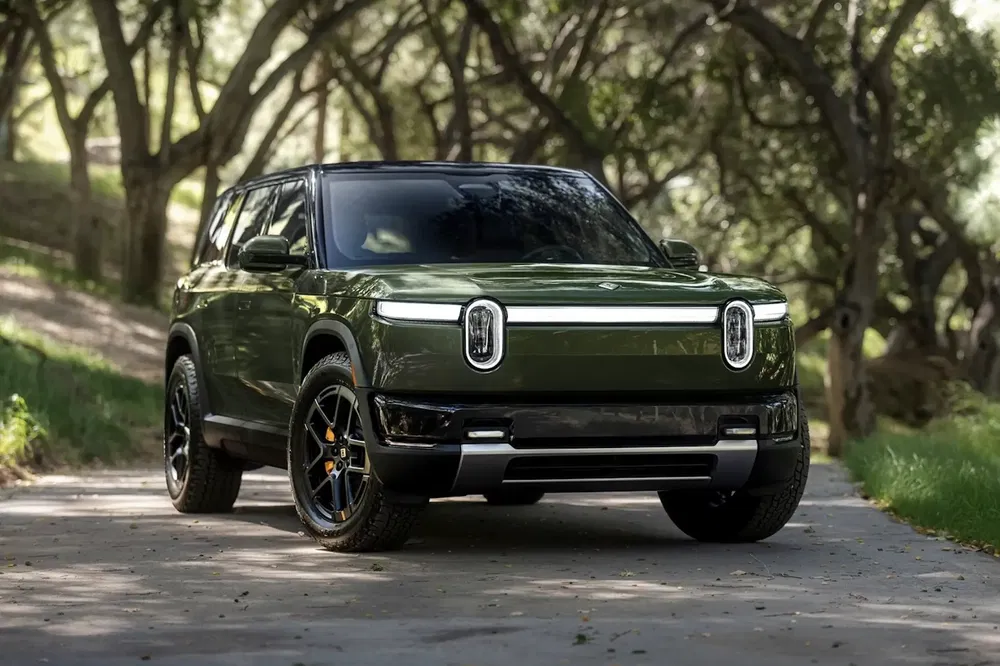 SUV électrique Rivian R1S vert en forêt, design robuste et moderne, stationné sur route.