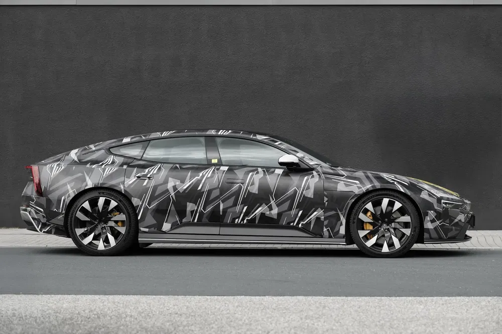 Prototype Polestar camouflé garé devant un mur gris, montrant design aérodynamique élégant.