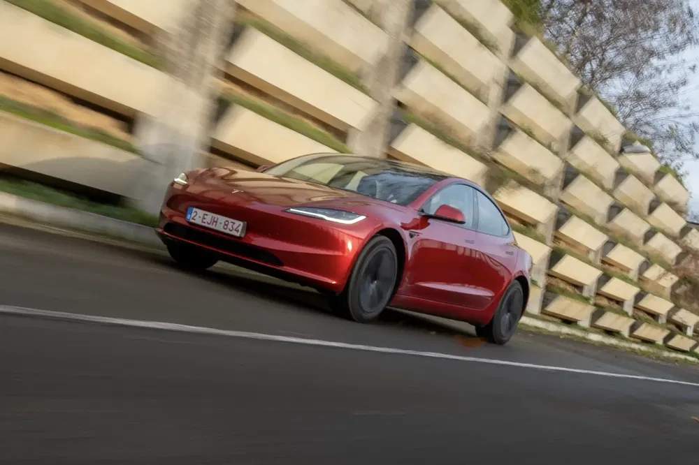 {"fr":"Tesla rouge Model 3 en mouvement rapide sur une route bordée de murs en béton.","nl":"Rode Tesla Model 3 rijdt snel langs een weg met betonnen muren."}