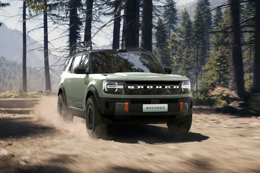 Ford Bronco roulant sur un chemin de terre en forêt, démontrant ses capacités tout-terrain.