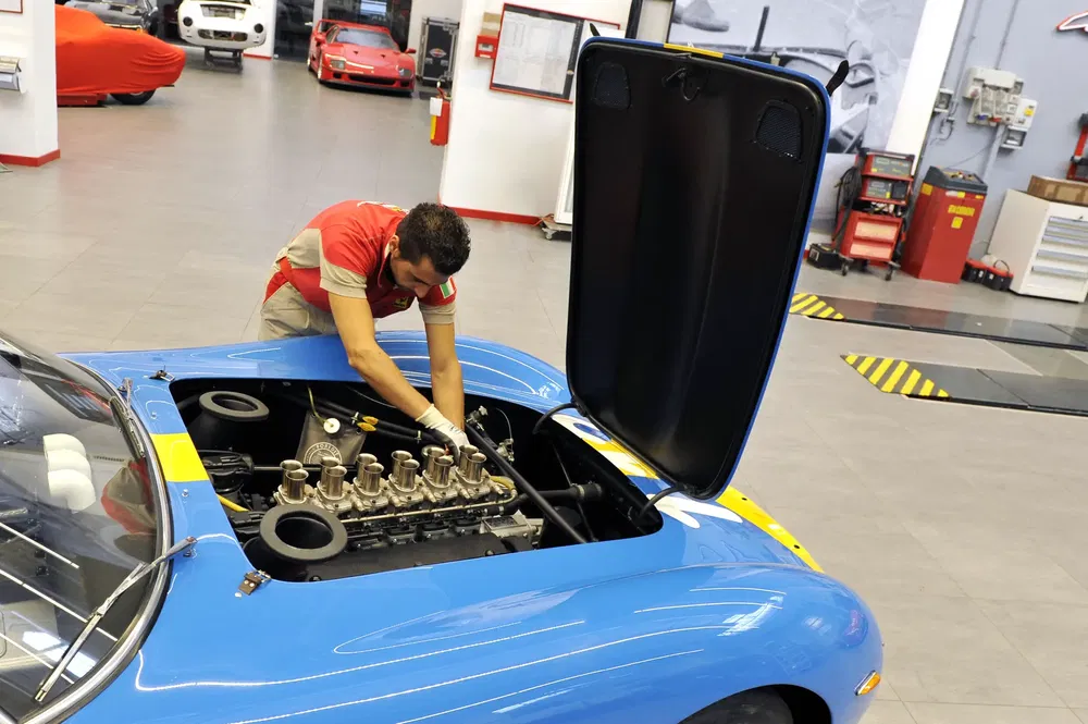 Technicien travaillant sur le moteur d'une vieille voiture de sport bleue dans un garage.