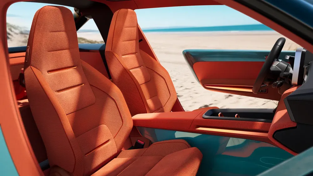 Interieur van een moderne auto met oranje stoelen en een strand op de achtergrond.