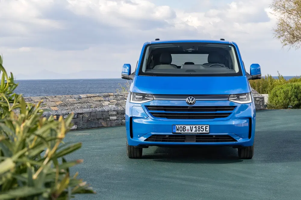 Blauwe Volkswagen Multivan voor een zeezicht met bewolkte lucht.