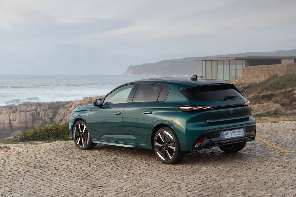 Groene Peugeot 308 geparkeerd aan zee, zicht op achterkant en zijkant.