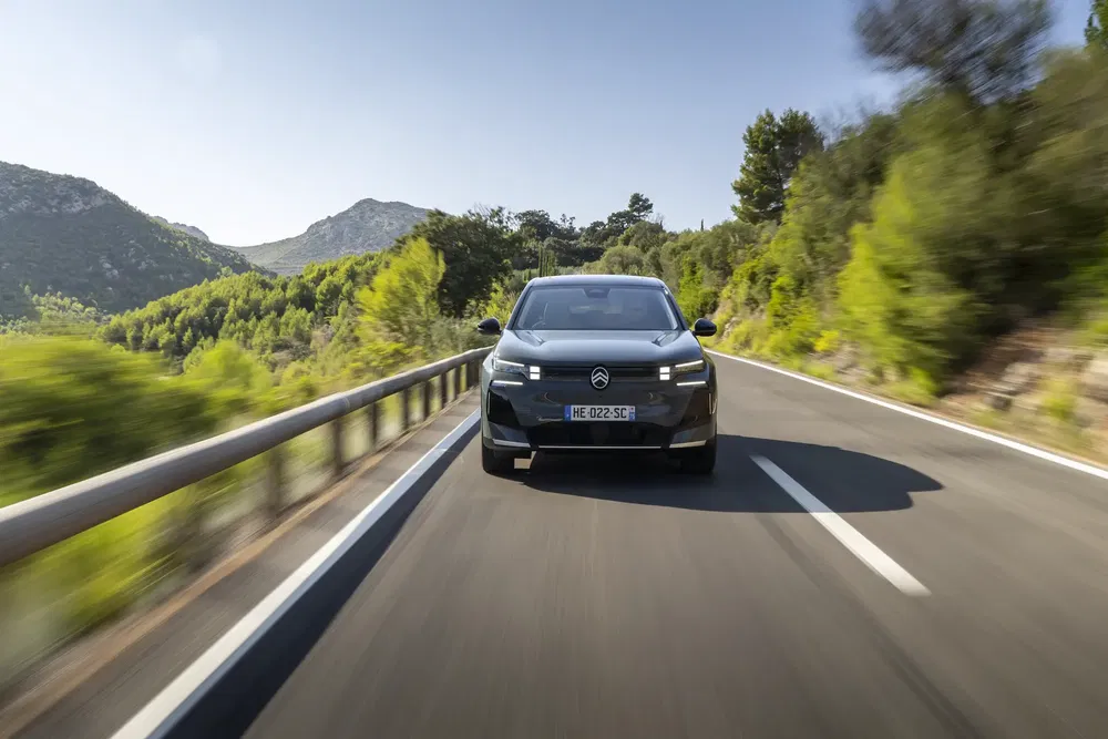 Citroën C5 X noir roulant sur une route de montagne bordée d'arbres verts.