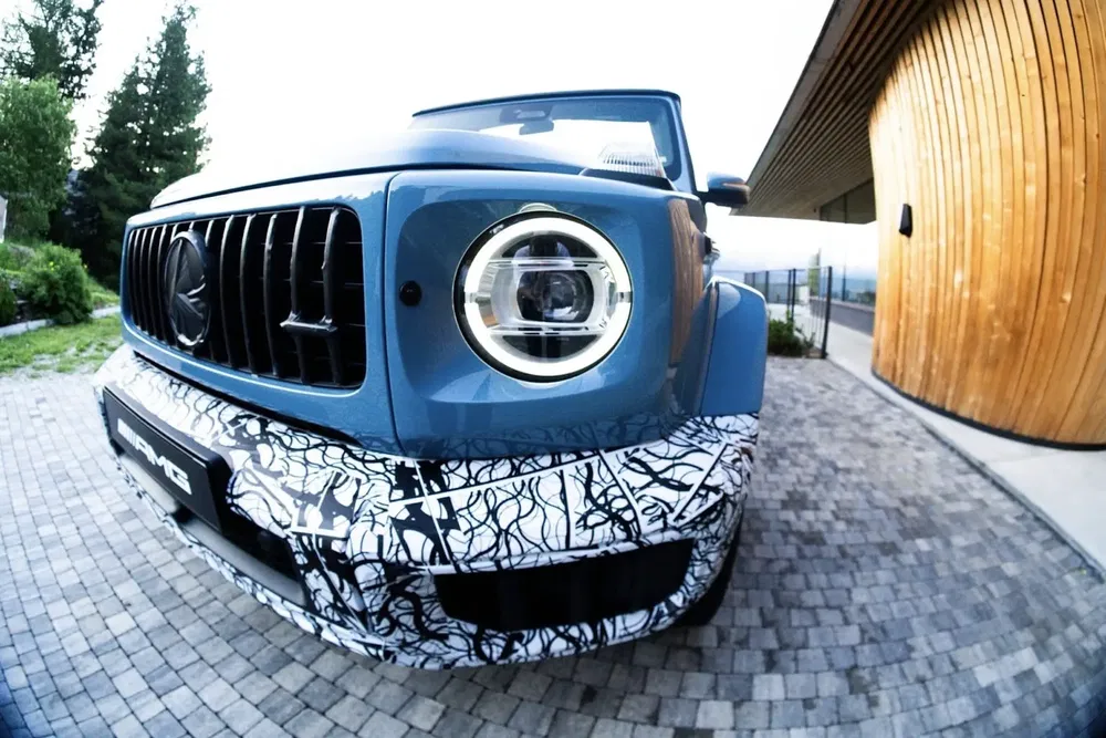 Mercedes-AMG G-Class bleu avec camouflage partiel sur une allée pavée.