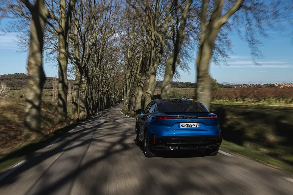 Blauwe Toyota Mirai rijdt op een met bomen omzoomde weg, heldere lucht.