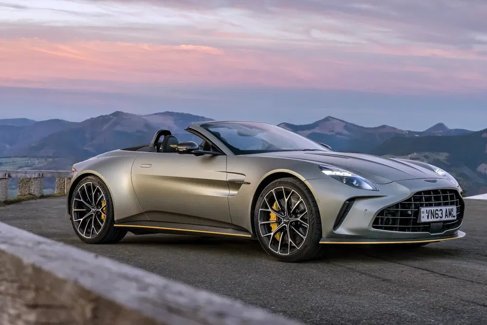Aston Martin DBS Volante gris sur route montagneuse au coucher du soleil.