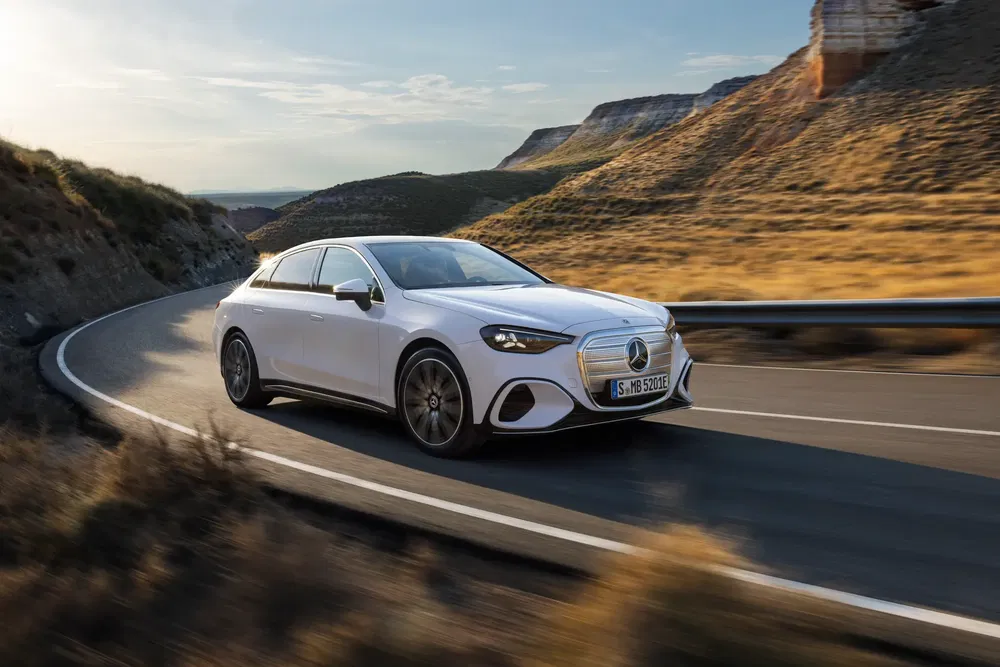 Mercedes-Benz E-Class blanche roulant sur une route sinueuse au coucher du soleil.