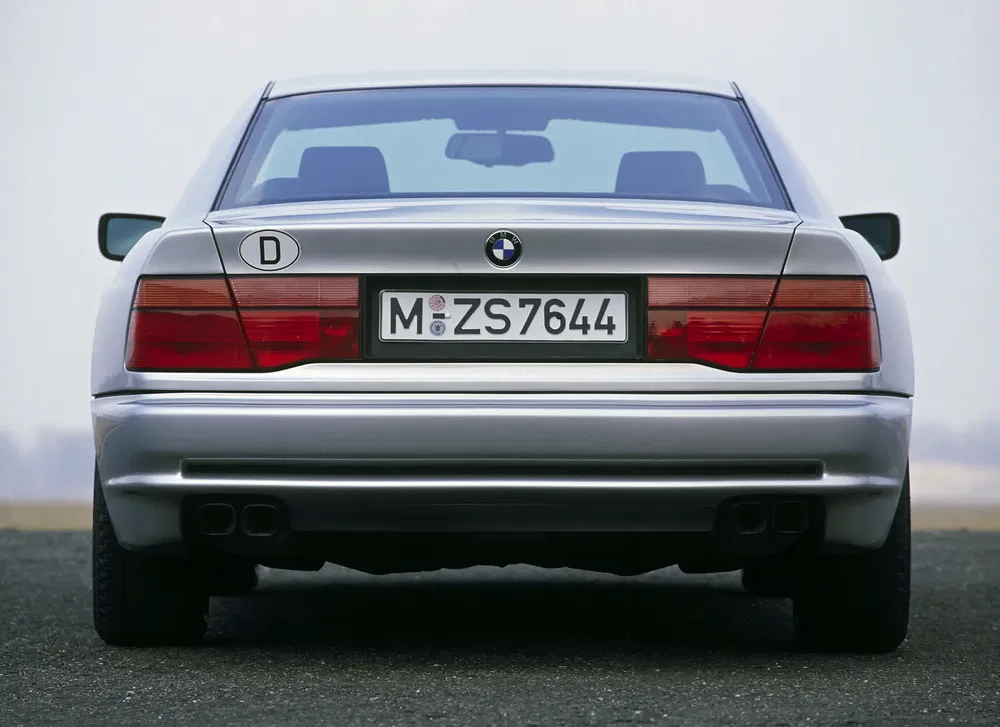 Vue arrière d'une BMW série 8 argentée avec plaque allemande, sur fond flou.