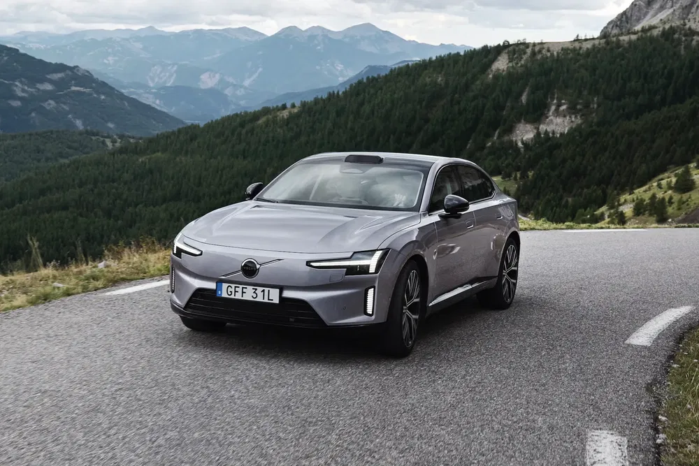 Volvo électrique roulant sur une route sinueuse de montagne, entourée de paysages pittoresques.