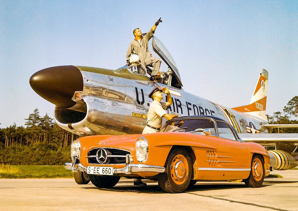 Mercedes-Benz 300 SL orange devant un chasseur US Air Force, pilote pointant vers le ciel.