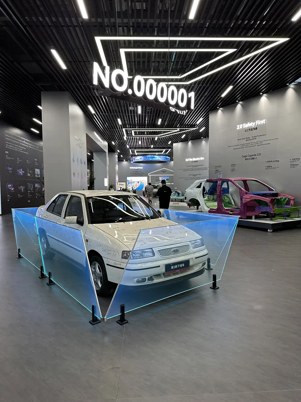 Witte Geely auto tentoongesteld in moderne hal met 'No.000001' display.