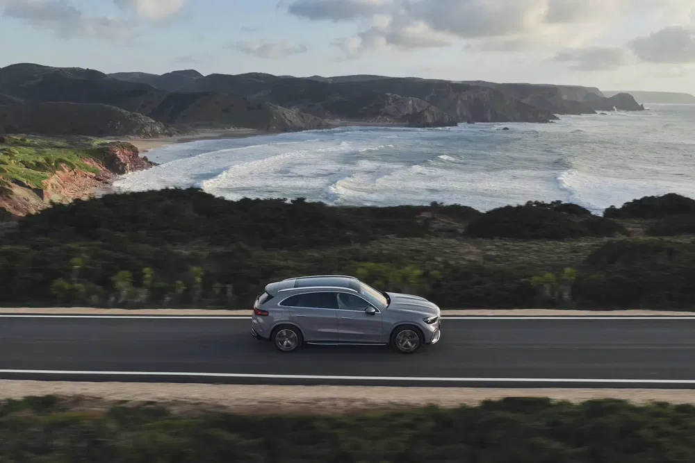 SUV Mercedes-Benz sur une route côtière panoramique avec océan et collines en arrière-plan.