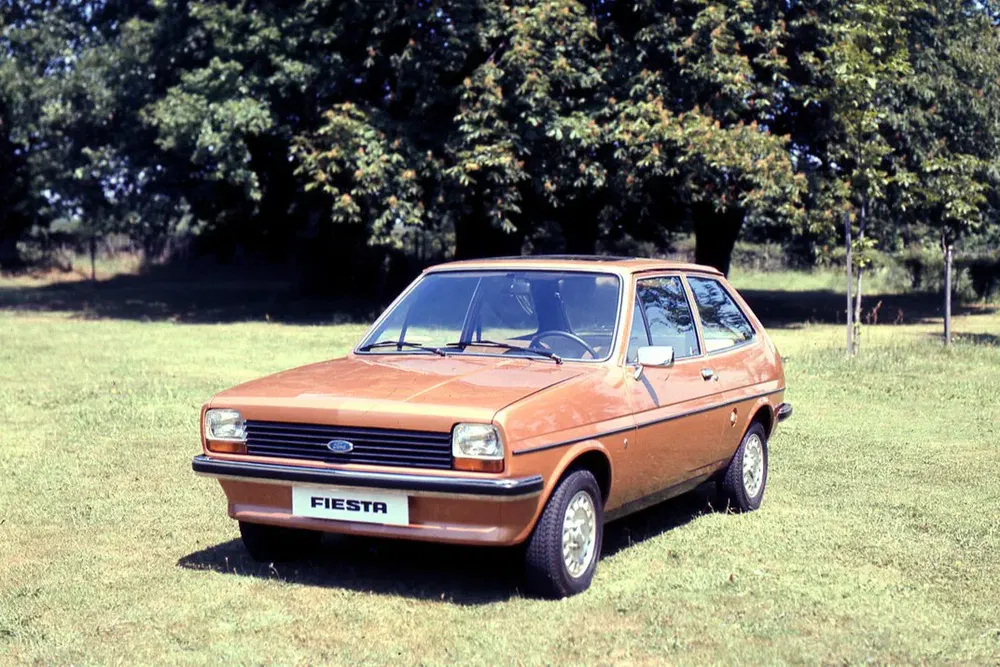 Ford Fiesta vintage marron sur pelouse verte, entourée d'arbres.