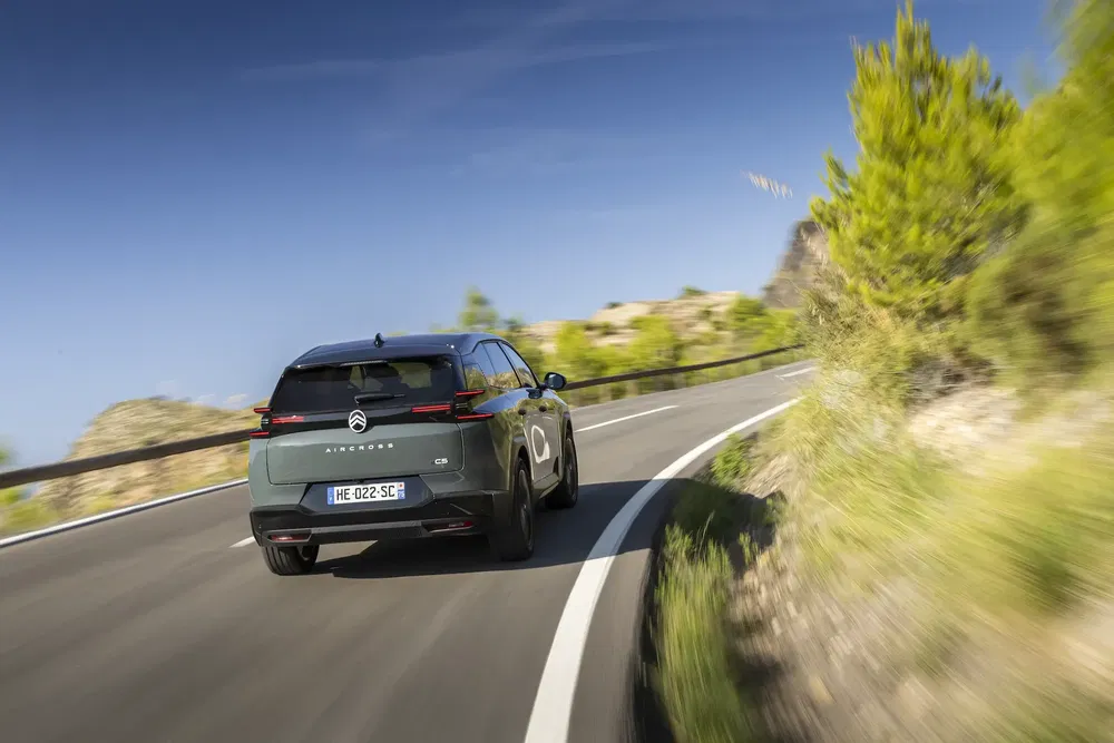 Citroën C5 X roulant sur une route sinueuse entourée de verdure sous un ciel bleu.
