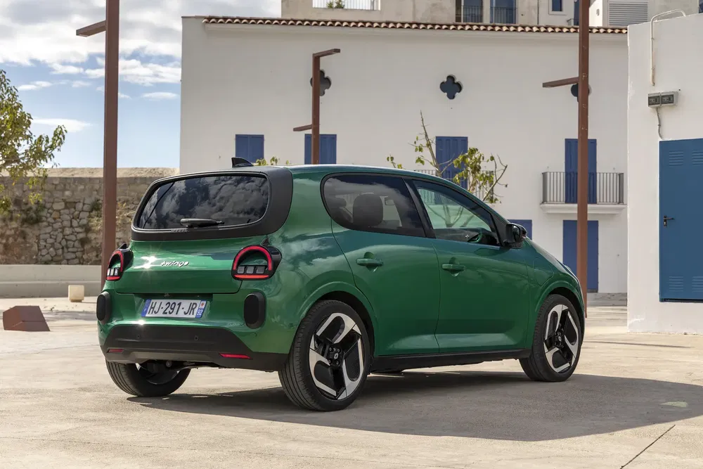 Citroën C3 électrique vert, design moderne, stationnée devant bâtiment blanc, ciel nuageux.