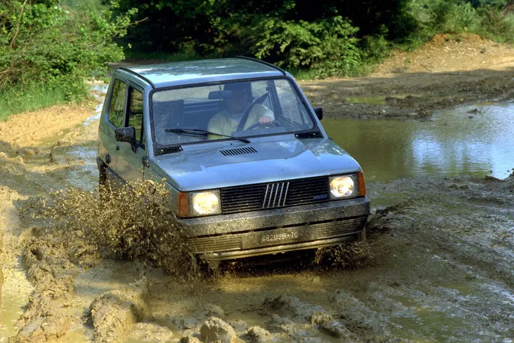 Fiat Panda rijdt door modderige bospad, opspattend water en modder.