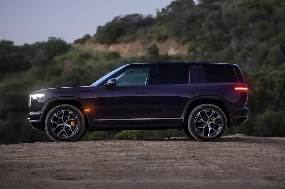 SUV Rivian R1S violet garé sur un chemin de terre, collines verdoyantes en arrière-plan.