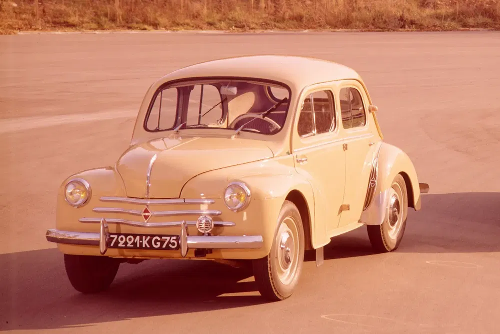 Voiture vintage Renault 4CV beige, stationnée sur une aire ouverte avec plaque d'immatriculation.