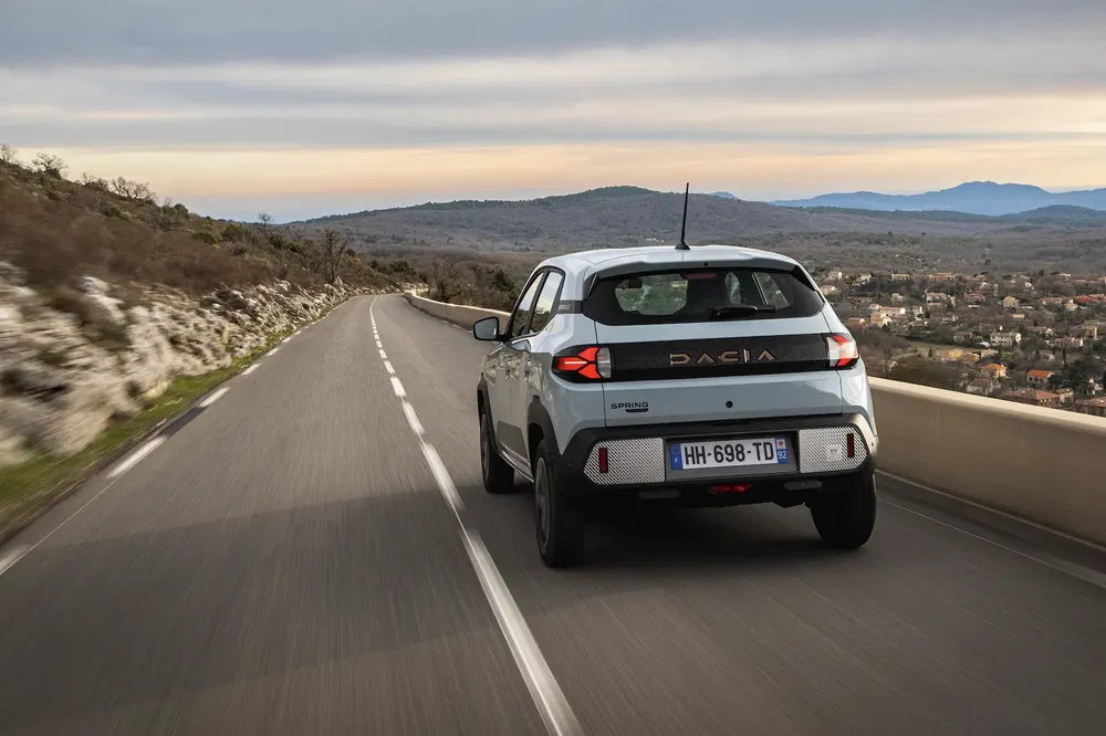 Dacia Spring rijdt op kronkelige bergweg onder bewolkte lucht.