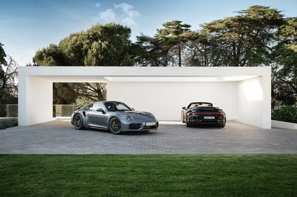 {"fr":"Deux voitures Porsche garées sous un abri moderne entouré de verdure.","nl":"Twee Porsche-auto's geparkeerd onder een moderne luifel omgeven door groen."}