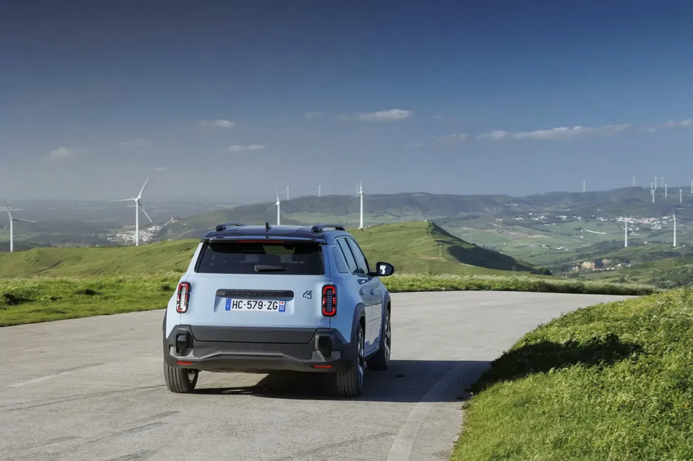 Mini Countryman op plattelandsweg met windmolens in de achtergrond, blauwe lucht.