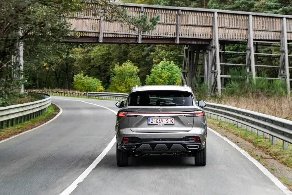 Achterzijde van een moderne SUV op een landelijke weg onder een houten brug.