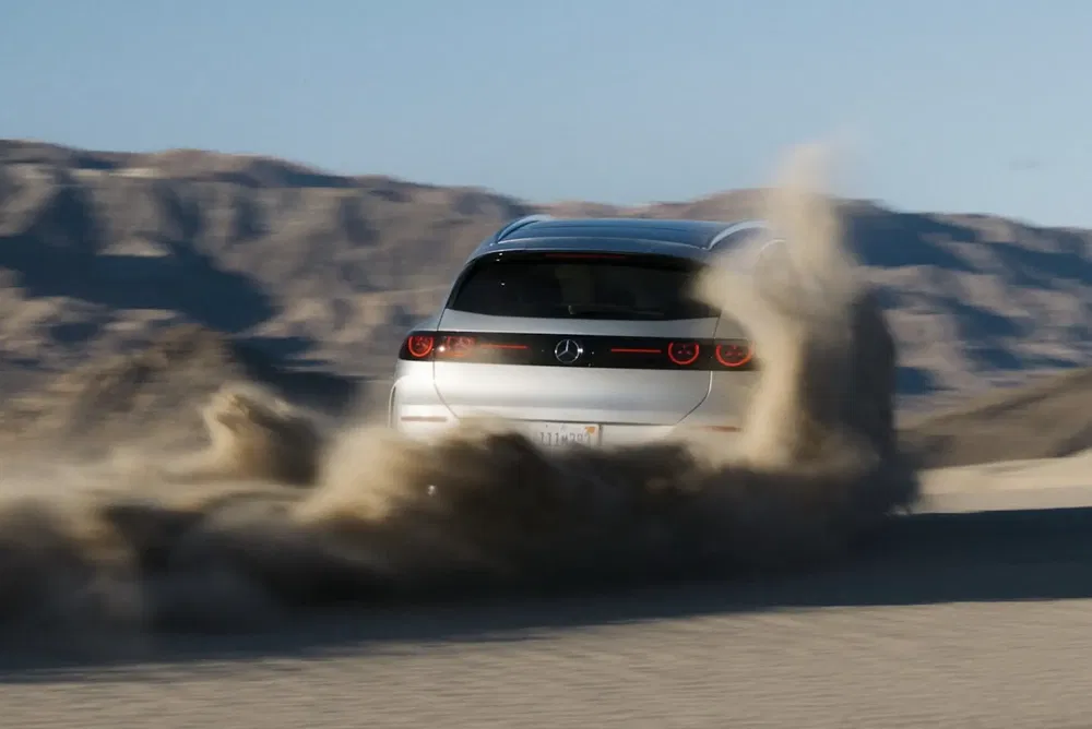 Voiture argente soulevant de la poussiere dans le desert, montagnes en arriere-plan.