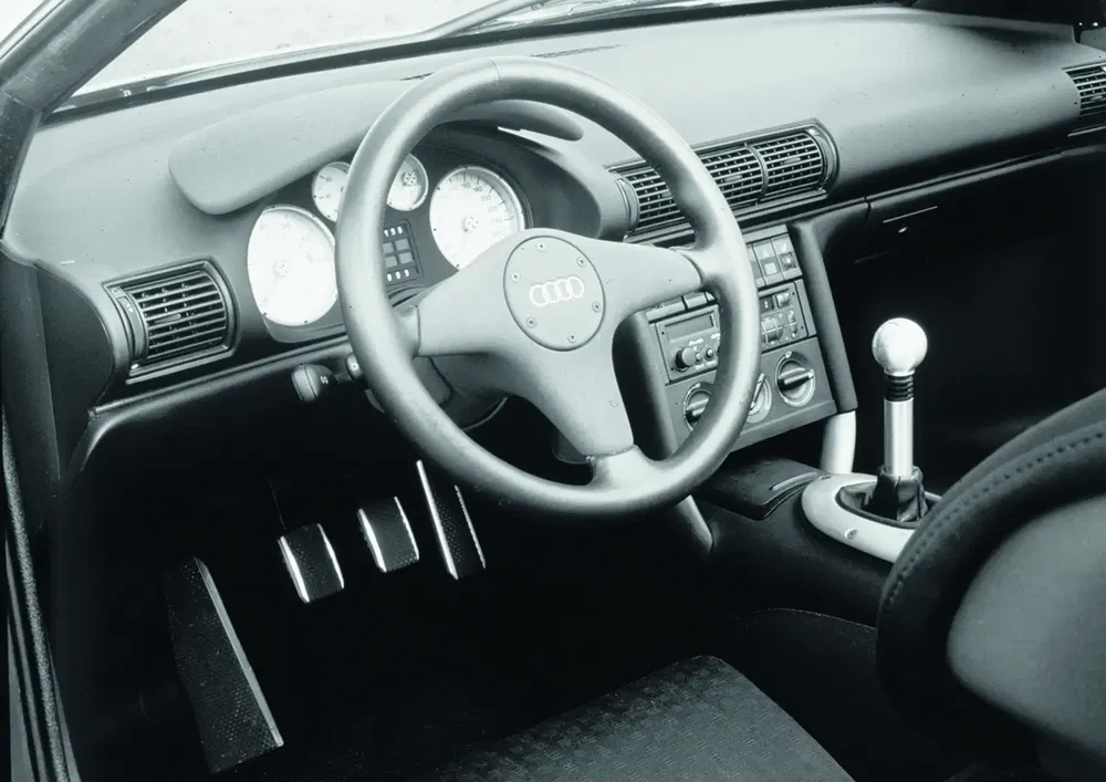 Vintage interieur van een Audi met drie-spaaks stuur en handmatige versnellingspook.