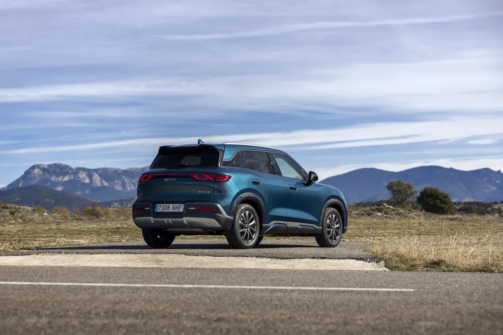 BYD ATTO 3 SUV bleu sur route montagneuse, ciel nuageux en arrière-plan.