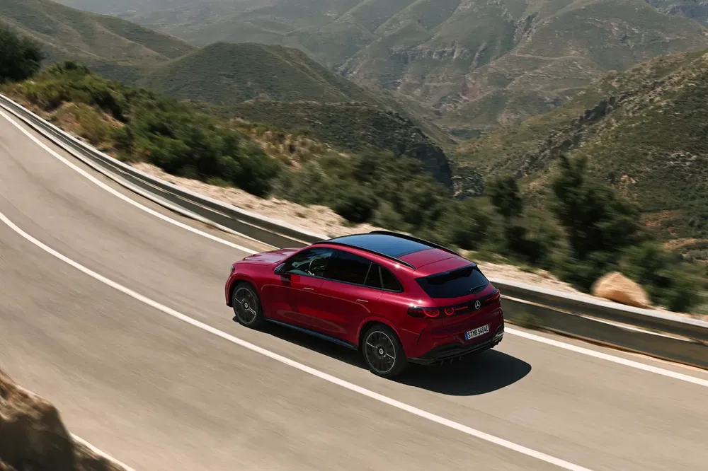 Mercedes-Benz rouge sur route de montagne sinueuse avec paysages verdoyants.