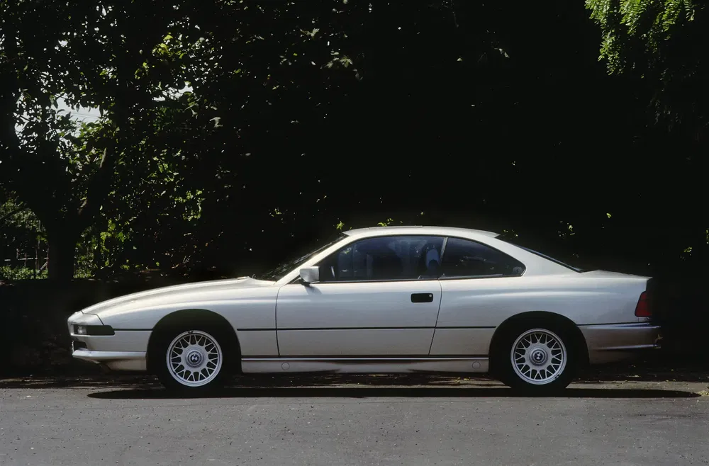 BMW 8 Series blanche garée, vue latérale, sous un arbre ombragé.