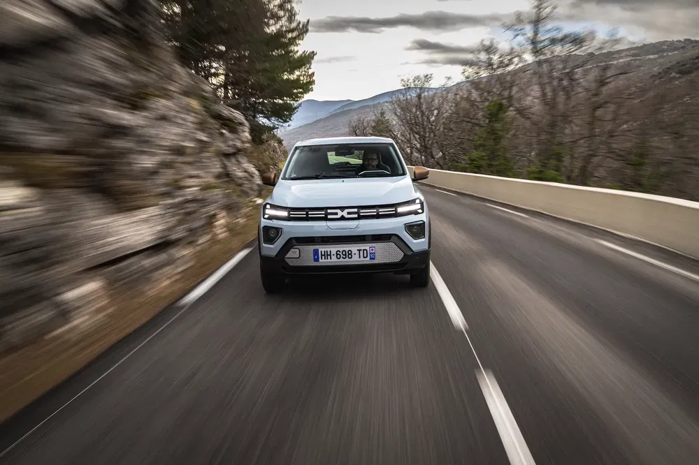 SUV met Dacia-badge rijdt op bochtige weg door bergachtig landschap.