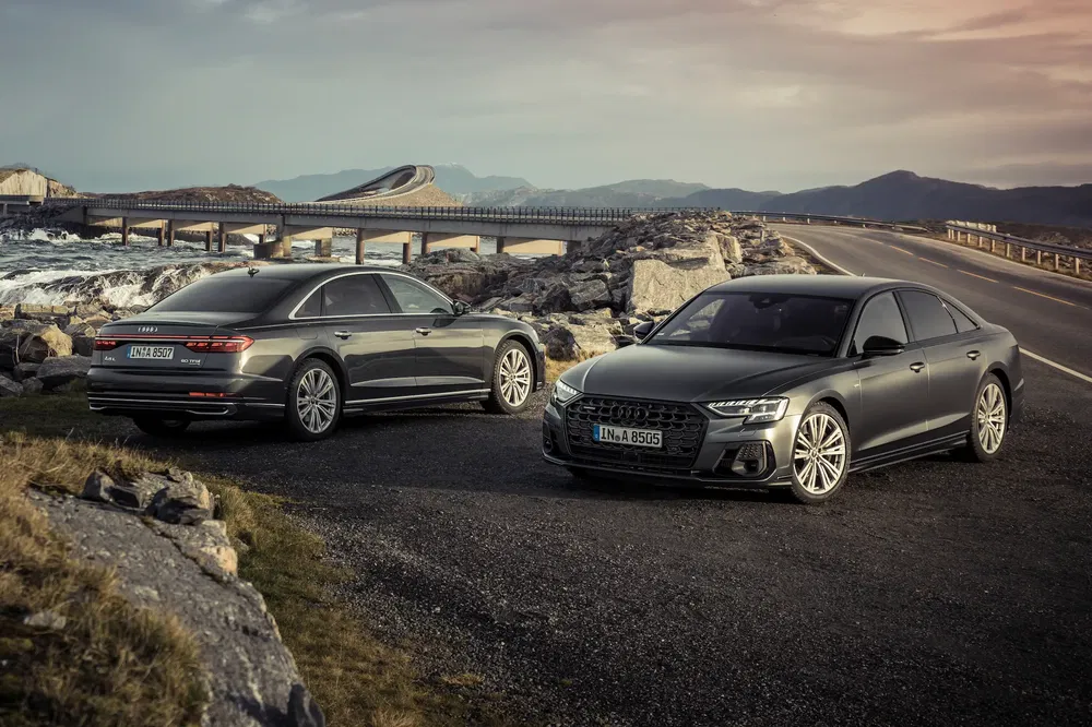 Twee grijze Audi A8's geparkeerd op een schilderachtige kustweg bij schemering.
