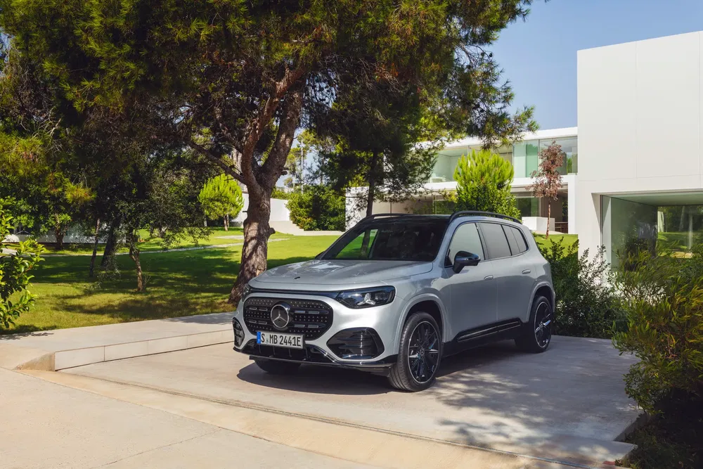 SUV Mercedes-Benz gris garé devant une maison moderne, entouré d'arbres et de verdure.
