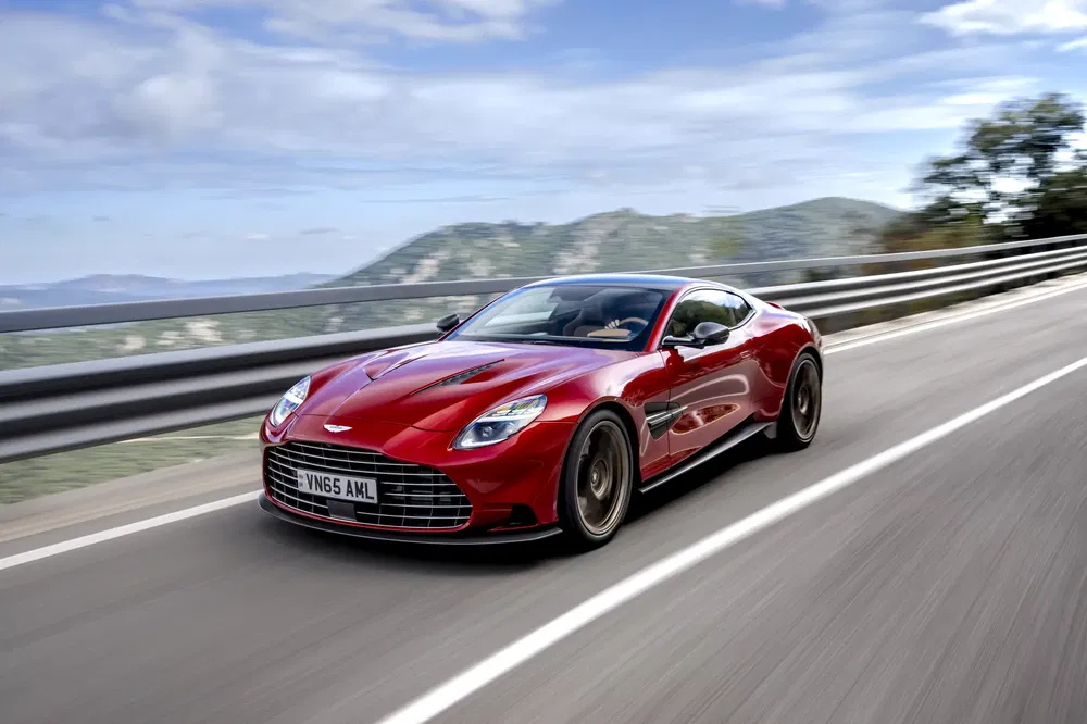 Aston Martin DB11 rouge roulant sur une route panoramique, montagne en arrière-plan.