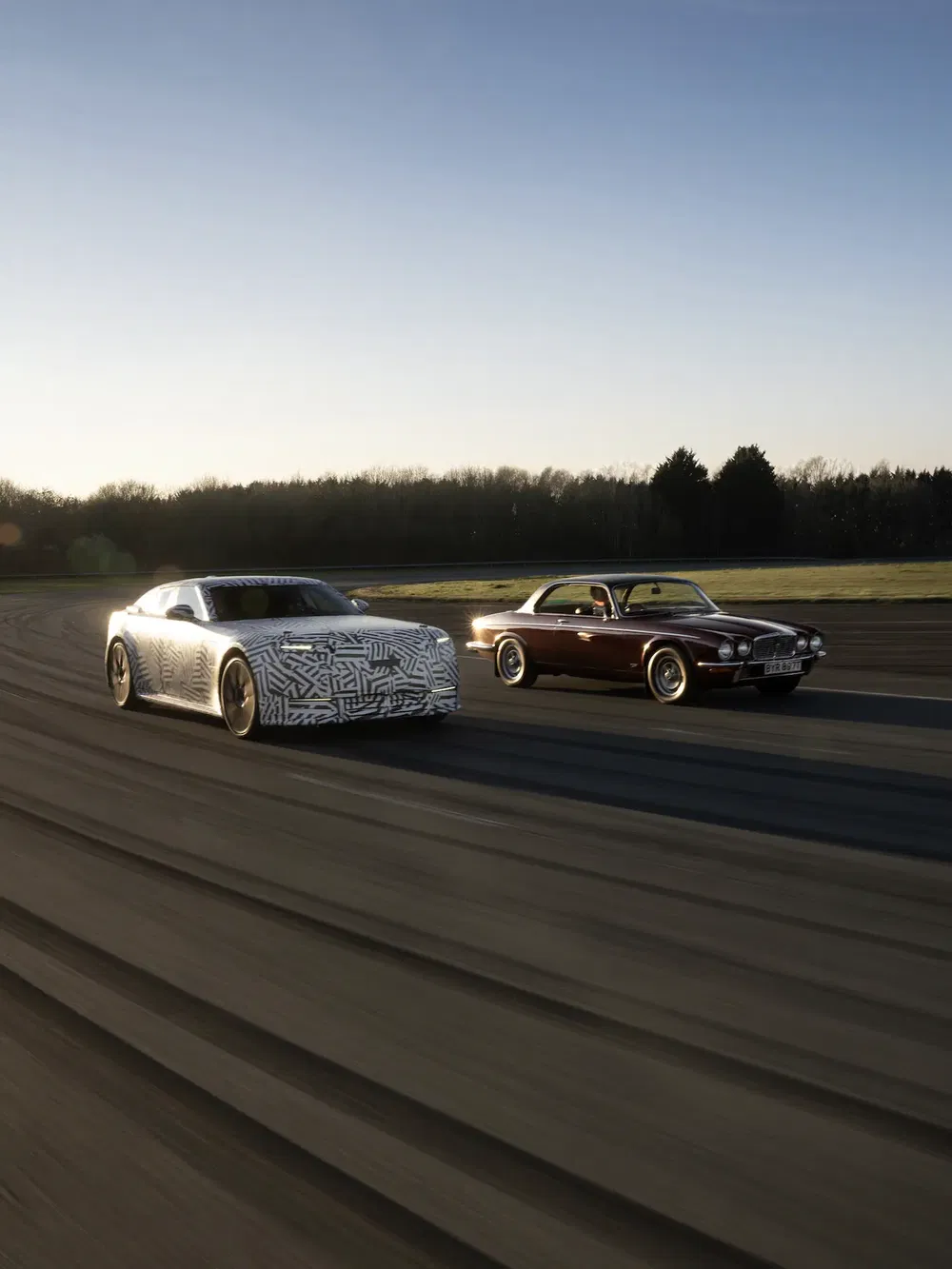 Moderne gecamoufleerde auto en klassieke Jaguar XJ-S rijden zij aan zij op circuit.