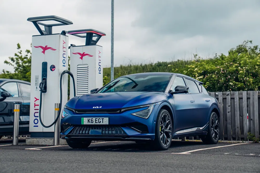 Voiture électrique Kia EV6 en charge à une station Ionity, ciel nuageux en arrière-plan.