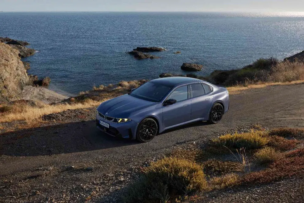 BMW M5 bleu stationnée en bord de mer sur une route côtière pittoresque.
