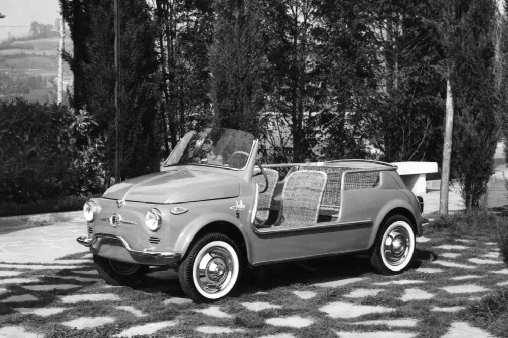 Klassieke Fiat 500 Jolly cabriolet met rotan interieur, geparkeerd in een aangelegde tuin.